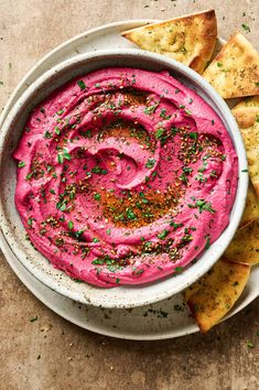 a white bowl filled with pink hummus and pita chips