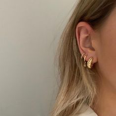 a close up of a person wearing gold earring and a white shirt with long hair