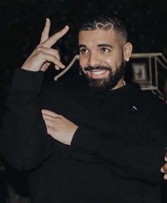 a man with a goatee smiles and holds his hand up in the air while wearing a black sweater