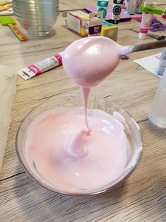 a pink liquid is being poured into a glass bowl on a wooden table with other craft supplies