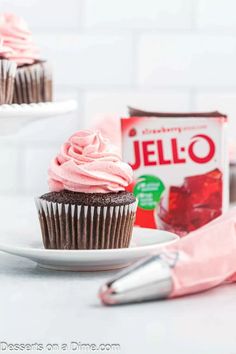 chocolate cupcakes with pink frosting on a plate next to a carton of jello