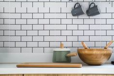 two wooden bowls and utensils sit on a kitchen counter with white subway tiles