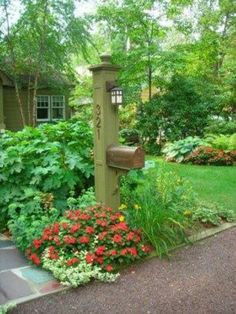 a mailbox surrounded by flowers and greenery in front of a house on a sunny day