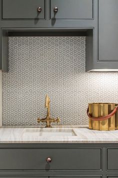 a kitchen with gray cabinets and gold faucet on the counter top next to a sink