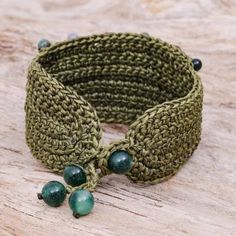 a close up of a bracelet on a wooden surface with green beads and bead