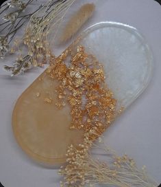 some gold flakes are sitting on a white surface next to dried flowers and plants