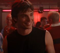 the young man is smiling and wearing a black tank top in front of other people