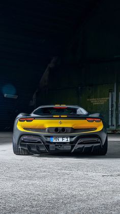 the rear end of a yellow sports car parked in a parking lot with dark background