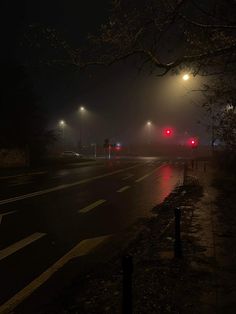 the street lights are red on a foggy night with no cars or people in it