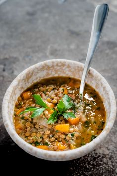 a white bowl filled with lentula soup on top of a stone counter next to a metal spoon