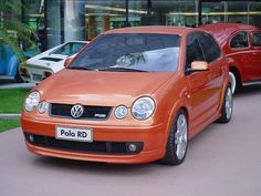 an orange car is parked in front of a red car on the side of the road