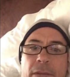 a man wearing glasses and a chef's hat is looking at the camera while laying in bed