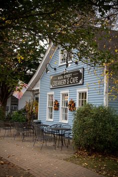 a blue building with tables and chairs in front of it on a brick sidewalk next to trees