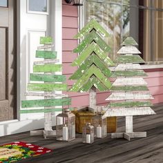 three wooden christmas trees sitting on top of a wood floor next to a pink house