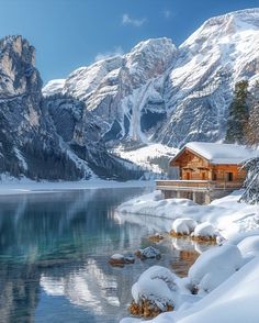 snow covered mountains surrounding a lake with a cabin in the foreground and water below