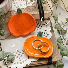 two wedding rings sitting on top of an orange pumpkin shaped plate next to a small potted plant