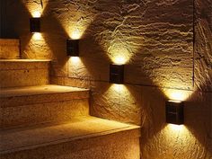 some lights that are on the side of a set of steps in front of a stone wall