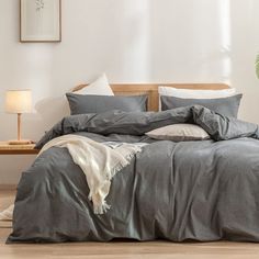 a bed with grey sheets and pillows in a room