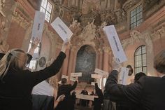 several people holding up signs in front of a building with statues on the walls and windows