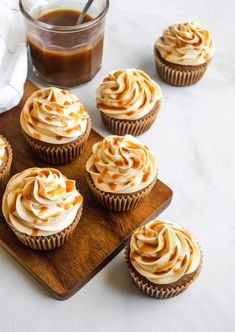 cupcakes with frosting and caramel on a wooden tray next to a glass of coffee