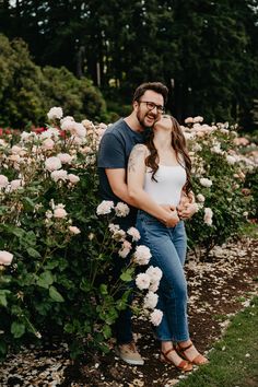 a man and woman standing next to each other in front of some flowers with their arms around each other