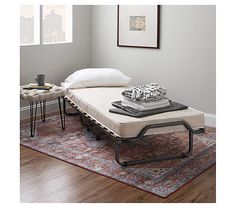 a bed sitting on top of a wooden floor next to a table with two pillows