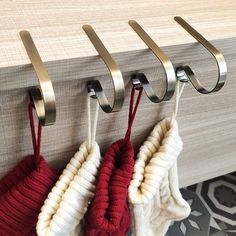 three knitted mitts hanging from hooks on a wall