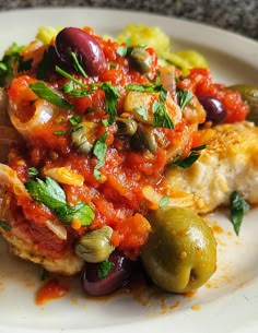 a white plate topped with meat covered in sauce and olives