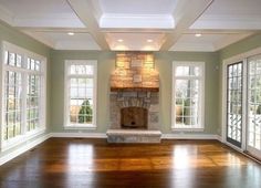 an empty living room with wood flooring and stone fireplace in the center surrounded by windows