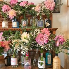 bottles and vases filled with flowers sit on a table in front of a fireplace