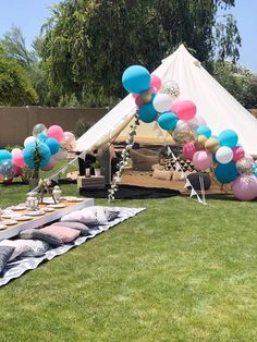 an outdoor party with balloons and pillows on the grass in front of a teepee tent