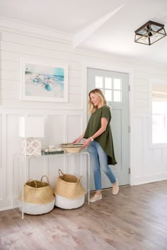 a woman standing in front of a white door with baskets on the floor next to her