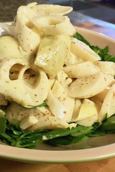 a bowl filled with pasta and lettuce on top of a wooden table