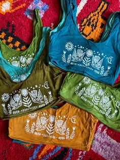 four women's tank tops with designs on them sitting on a colorful rug in the sun