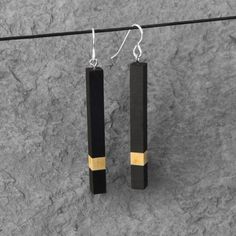 pair of black and gold earrings hanging from a wire on top of a stone surface