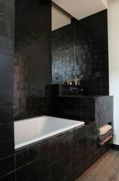 a black tiled bathroom with a white bathtub