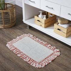 a white rug with pink ruffles on the floor in front of a wooden cabinet