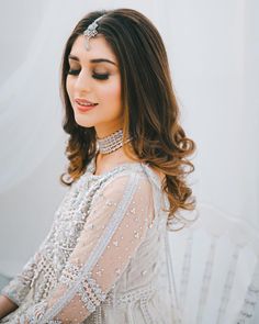 a woman with long hair wearing a white dress and headpiece in front of a wall