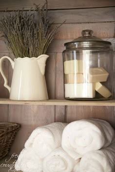 towels are stacked on the shelf next to a pitcher and glass jar with lavender in it