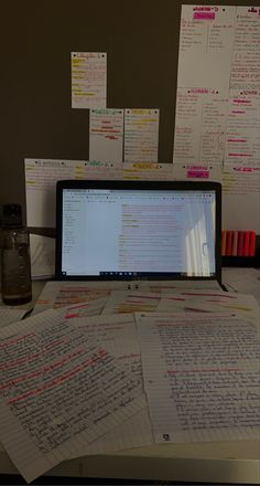 an open laptop computer sitting on top of a desk covered in lots of writing paper