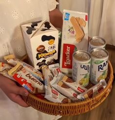 a person holding a wicker basket filled with snacks and milks in front of a white curtain