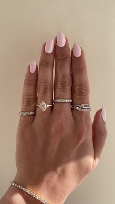 a woman's hand with pink manicured nails and three different rings on it