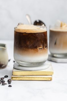 two glasses filled with liquid and topped with chocolate chips on a white surface next to a gold coaster