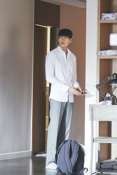 a man standing in front of a book shelf with a backpack on the floor next to him