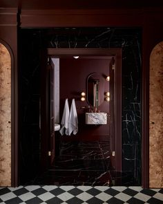 a black and white checkered floor in front of a bathroom with red walls, marble counter tops and an open door