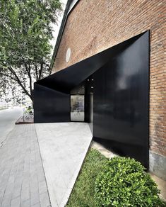 an open door on the side of a brick building with grass and trees around it