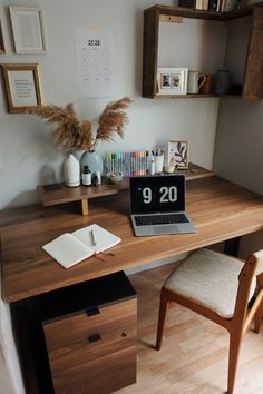 a laptop computer sitting on top of a wooden desk next to a book and pen