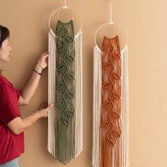 a woman standing next to two wall hangings with macrame beads on them