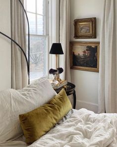 a bed with white sheets and pillows in front of a painting on the wall next to a window