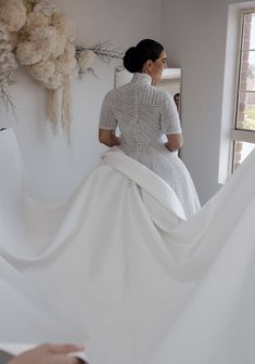 a woman in a white dress is standing near a window and looking at something on the wall